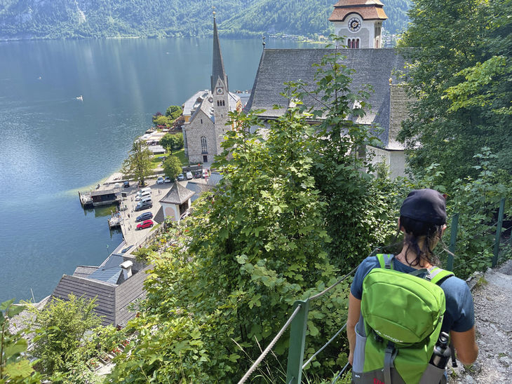 Wanderer blickt auf Hallstatt und den See von einem bewaldeten Hang aus.