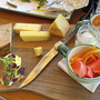 Käseplatte mit Brot, Gemüse und Aufstrichen auf einem Holzbrett.