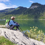 Wanderer sitzt mit Rucksack am Ufer des Schwarzensees im Salzkammergut.