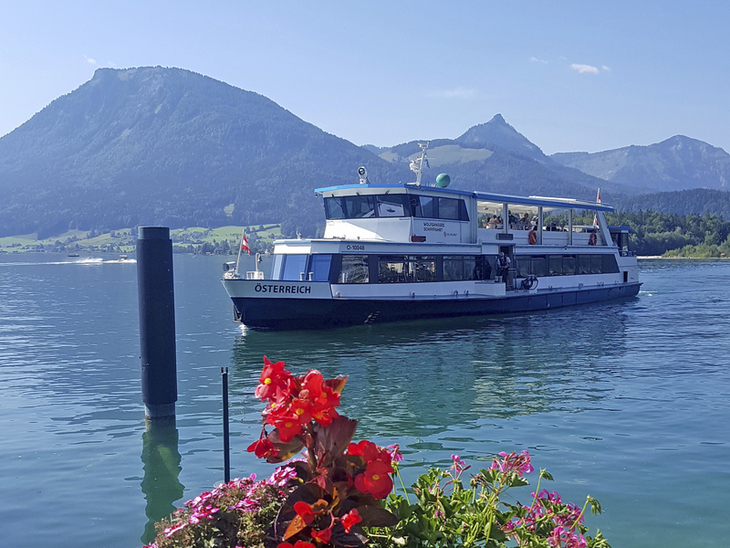 Schiff auf dem Wolfgangsee mit Bergen im Hintergrund und Blumen im Vordergrund.